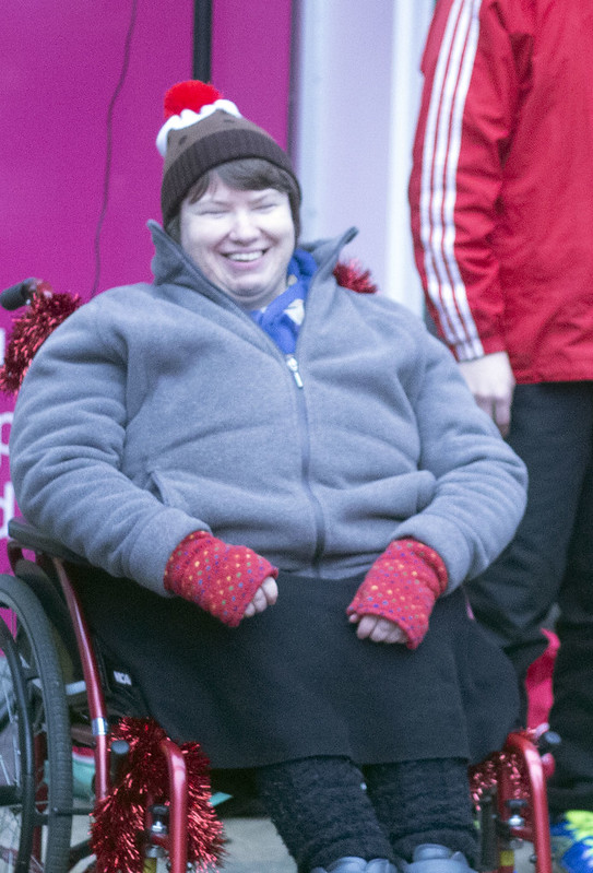 Woman sits in wheelchair with red fingerless gloves and a Christmas pudding hat