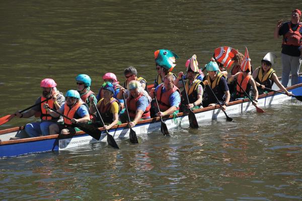 A team of rowers with fish themed hats row on the river in a longboat