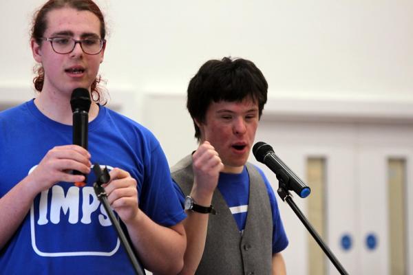 Two members of IMPs sing on a stage wearing blue IMPs t-shirts