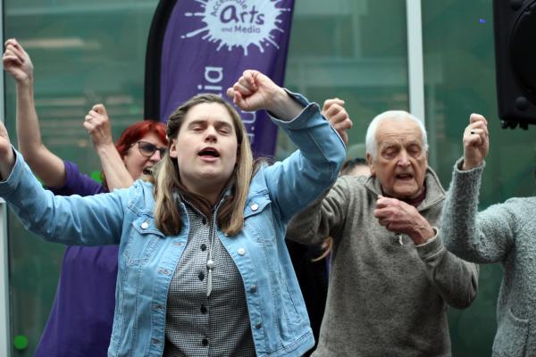 Three people stand with their hands in the air as they sing