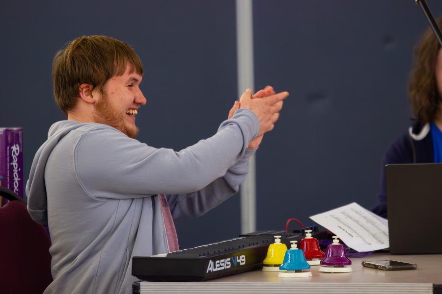 A young man sitting in front of a keyboard and smiling at his band mates 