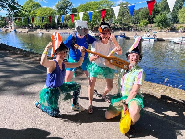 Four people pose with an oar shaped trophy whilst wearing fish themed hats