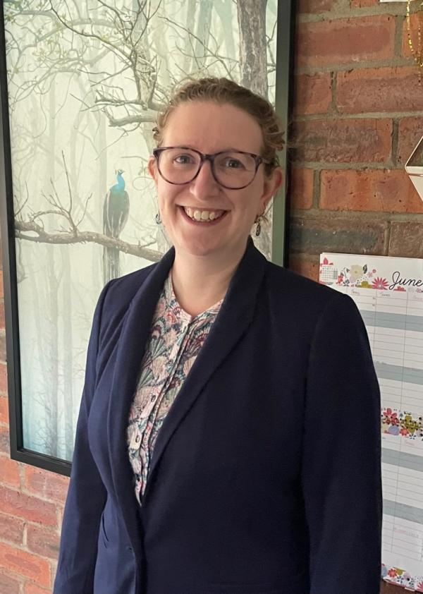 Jenny Anderson stands against a brick wall wearing glasses 
