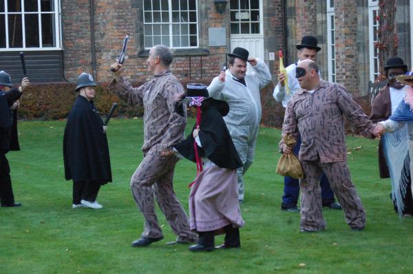 Performers dressed as cops and robbers chase each other on a lawn